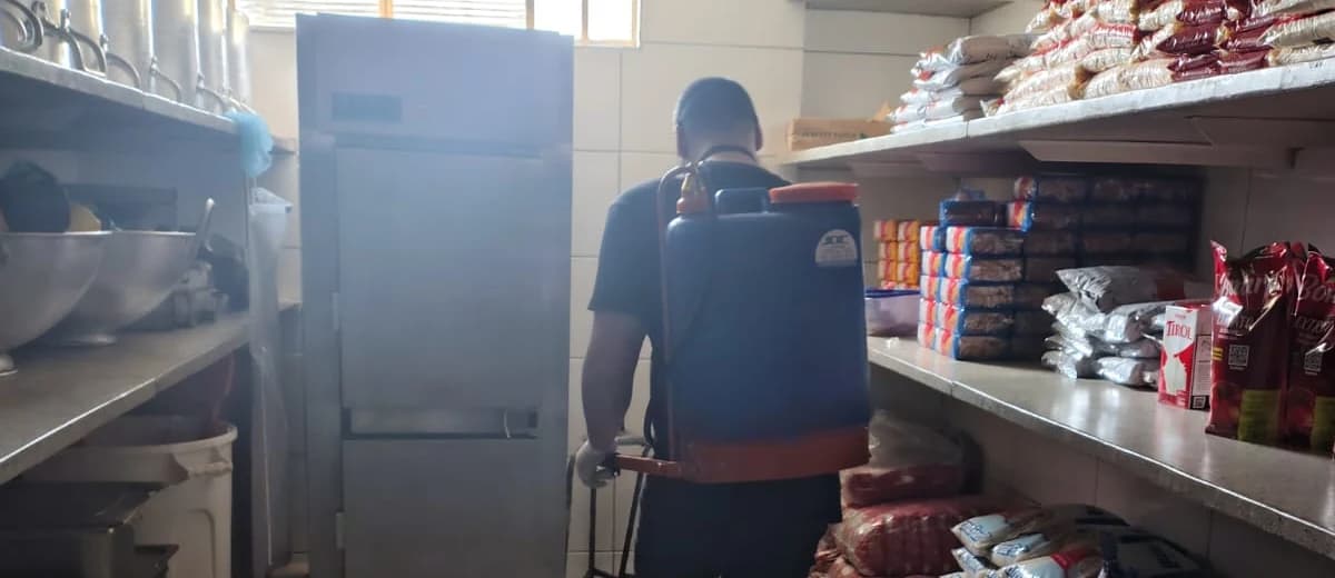 Profissional com bomba costal em corredor de estoque com prateleiras de alimentos